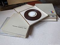 Seven Ampex branded white cardboard cases containing 1/4 inch audio tape reels, some cases open showing brown magnetic tape reels inside
