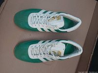 Top view of Adidas Franz Beckenbauer soccer shoes in green and white on cardboard background.