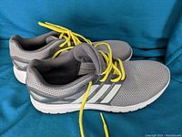 Pair of Adidas running shoes side view showing grey mesh material, white stripes, and yellow laces.