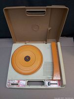 Open phonograph turntable showing orange turntable platter, tonearm, speed slider, and speaker grill.