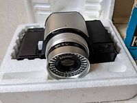 Close-up of Fotochrome camera in white foam packaging showing lens details and camera body.