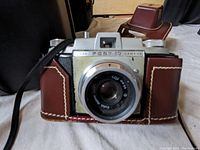 Front view of Kodak Pony IV camera in brown leather half-case with prominent lens and visible brand markings.