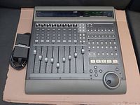 Front view of control surface showing 8 faders, buttons, jog wheel and included power adapter