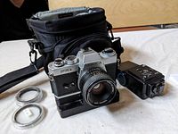 Yashica FR II camera with lens attached, battery winder grip underneath, two lens filters in front, and external flash positioned to the side. All items on white surface.