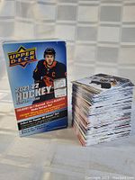 Photo shows original Upper Deck 2021-22 Series One hockey card box standing upright next to a tall stack of hockey base cards from the set.