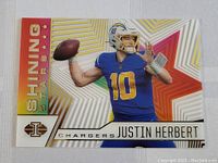 Front close-up of Justin Herbert Shining Stars football insert card showing reflective gold foil star and blue Chargers uniform with number 10.