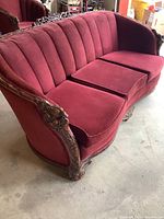 Full view of the antique three-seater couch showing red velvet upholstery and wooden carved details along sides and bottom.