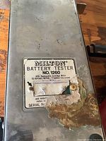 Close-up of label on metal casing showing brand Multon, model 1260, instructions for replacing cartridge and meter, and serial number area with rust damage.
