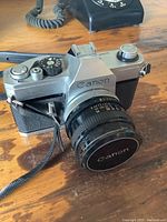 Front and side view showing Canon branding, lens with focus and aperture rings, and camera strap attachment.