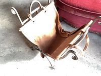 Metal and leather firewood cradle shown at an angle highlighting leather sling and curved metal frame