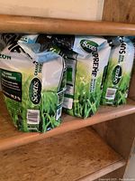 Three sealed Scotts Supreme grass seed bags on wooden shelf, side view