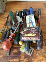 Photo showing assorted hand tools including screwdrivers, stapler, flashlight, and box of staples on wooden surface