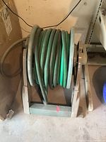 Green rubber garden hose coiled on beige/brown plastic cradle-style hose reel, showing front view with hose wound around reel.