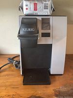 Front view of Keurig coffee maker showing its black and silver design, control panel, and coffee package on top.