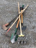 Full view of all five tools laid on gravel surface showing axe, hoe, shovel, hand rake, and edging tool.