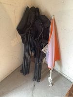 Multiple folded lawn chairs and a collapsible lounger with canopy leaning against a wall in corner