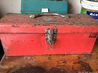 Closed red metal toolbox with silver latch and handle, showing worn and used condition