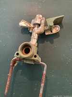 Close-up top view of the vintage metal impact sprinkler showing rusted metal legs and rotating nozzle with green paint.