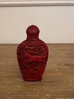 Front view of the red cinnabar snuff bottle showing carved horse and foliage with basketweave background.
