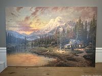 Full view of oil painting showing the mountains, lake, cabin, and trees landscape scene.