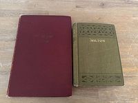 Two antique books side by side on wooden surface, one green with gold 'MILTON' lettering, one in dark red slipcover