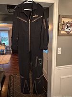 Full view of the black Royal Canadian Air Force 1968 vintage flight suit on hanger showing front zipper and several zippered pockets.
