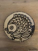 Full view of round ceramic plate with stylized black fish on cream background and dotted border.