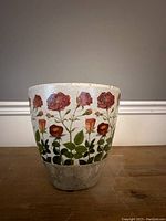 Front view of antique round white vase with hand painted roses and leaves, sitting on wood surface.