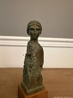 Full view of carved wooden bust sculpture standing on a flat surface with plain background.