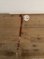 Full view of rosary with red beads, small container with religious statues, and two religious pendants on wooden surface.