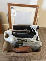 Wide view of assorted picture frames stacked inside a cardboard box on the floor.