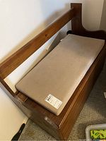 Side view photo of wooden bench with beige cushioned seat and backrest beam.