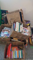 Photo of three cardboard boxes filled with assorted children's books and educational books, showing various titles and colorful covers.