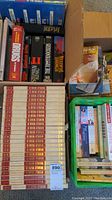 Books boxed and some stacked showing titles including World War II Encyclopedia set and fiction novels.