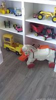 Shelf with multiple vintage-style toy vehicles including a yellow toy truck, a red wagon, and a pull-along white horse with red wheels.
