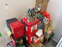 Stack of multiple Christmas collectible boxes including illuminated village houses and porcelain houses in various branded boxes.