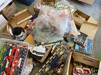 Overview of multiple Christmas wrapping paper rolls, assorted bows, ribbons, placemats, and holiday decor in boxes and plastic bags.