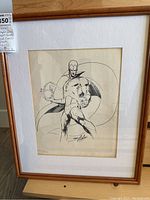 Framed portrait of superhero with swirling energy, wood frame and matting visible