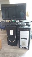 Two tower computers positioned side by side with a black keyboard and a black monitor on top of one tower, wired mouse also present