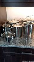 Full set of six Advancia stainless steel cookware pieces on countertop including large pots with lids and tall pasta pot.