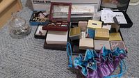 Full view of assorted jewelry including multiple boxes, necklaces, and pouches on carpeted floor.