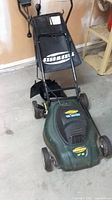 Full view of corded electric lawn mower with grass catcher attached, showing handle and wheels.
