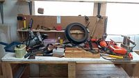 Photo showing workbench with power tools, hand tools, and accessories spread across the surface in used condition.