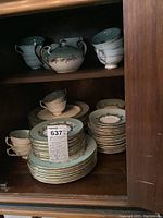 Cabinet shelf with stacked plates, cups, saucer and covered sugar bowl visible