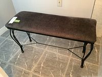 Bench with brown velvet-like upholstery and black metal curved legs, set on tiled floor.