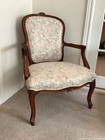 Front angle view of vintage armchair showing carved wooden frame and fabric upholstery.