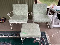 Two painted steel chairs and one ottoman with light green vinyl cushions with white leaf pattern, showing paint chips and oxidation on frames.