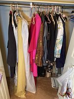 Full view of closet clothing including dresses, jackets, sweaters hung on hangers.