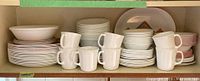Wide view showing stacked plates, bowls, and mugs in the shelf cabinet, showcasing multiple patterns and plain white mugs.