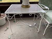 White painted steel end table with mesh metal top, curved legs, and decorative scrollwork beneath the tabletop. Shows oxidation.